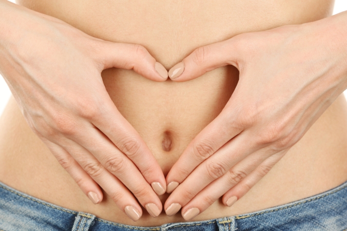 Close up of woman's tummy with her hands making a heart shape in front