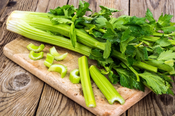 Chopped celery and celery stalks on a wooden chopping board